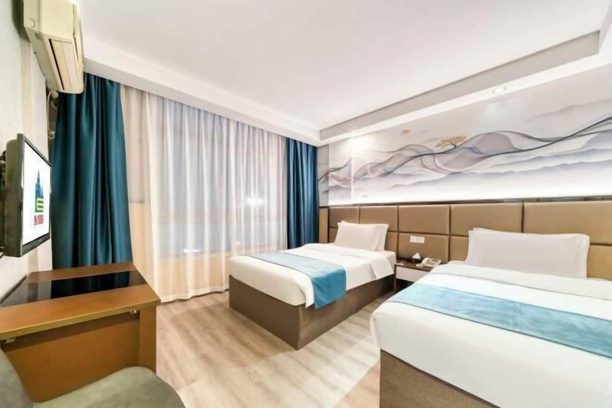 Une chambre d’hôtel avec deux lits, un bureau, une télévision et une grande fenêtre avec des rideaux.