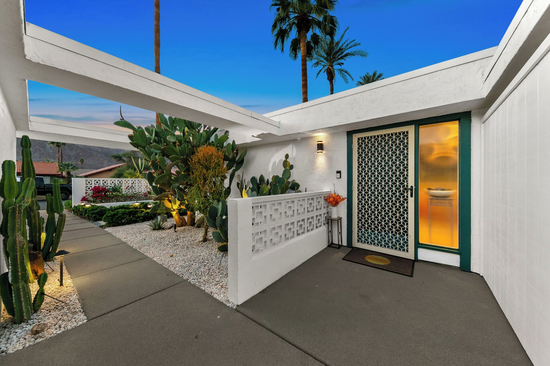 A modern house with a white exterior, a glass door with a geometric pattern, and a cactus garden.