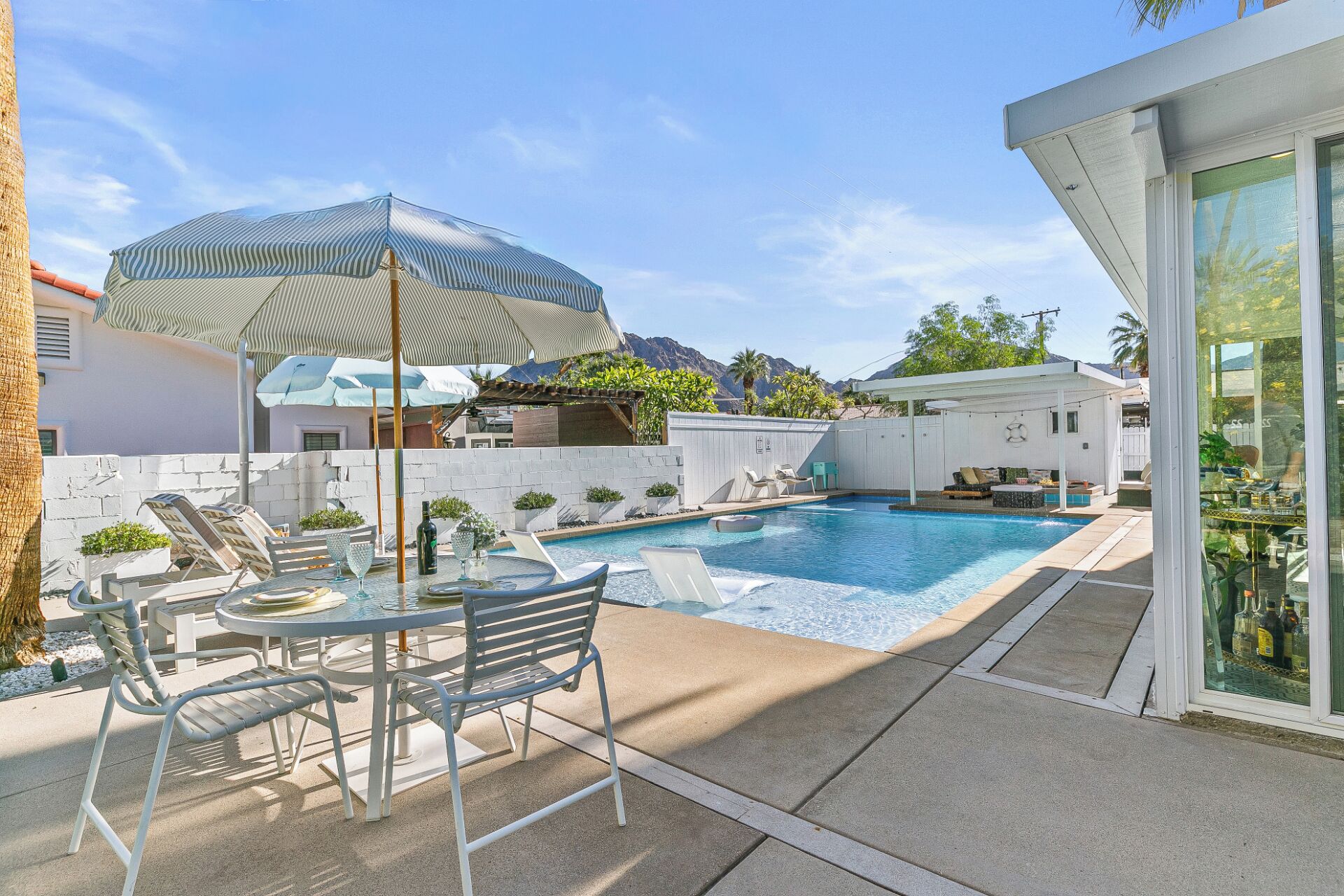 A backyard with a swimming pool, lounge chairs, and a table with chairs.