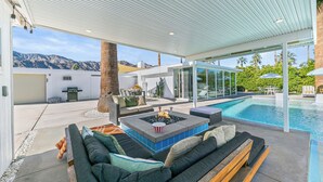 Un espace de vie extérieur moderne, doté d’une piscine, de coins salon et offrant une vue sur les montagnes.