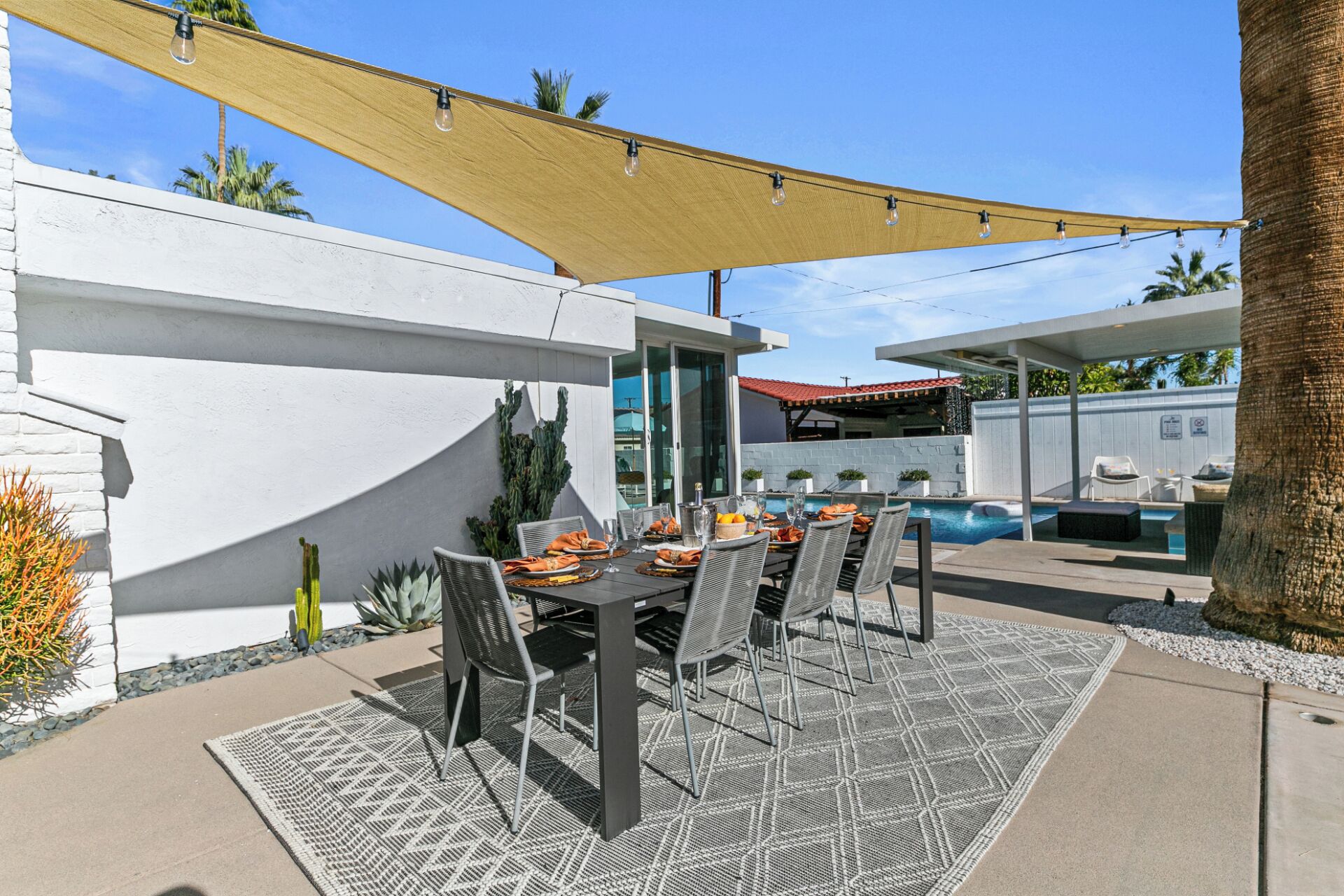 An outdoor patio with a pool, dining table, and chairs.
