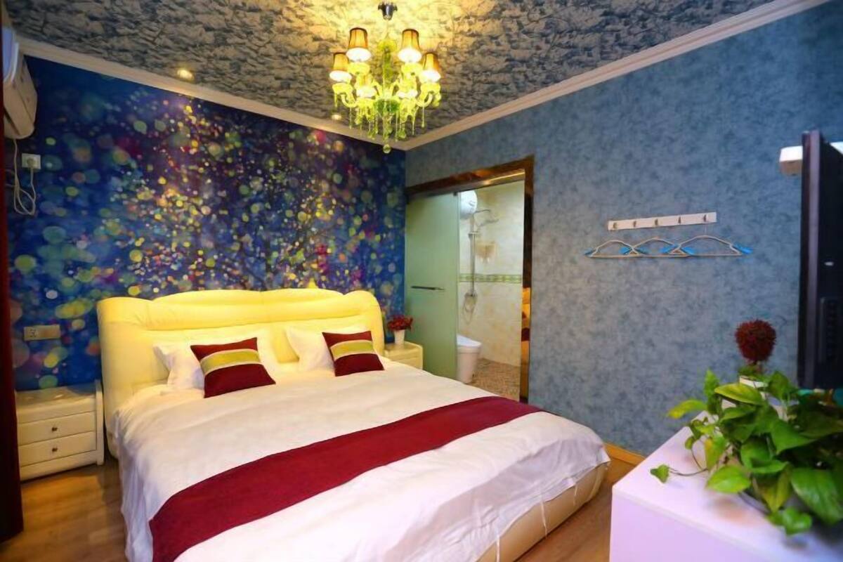A bedroom with a large bed, a chandelier, a blue wall with a floral pattern, and a mirror.