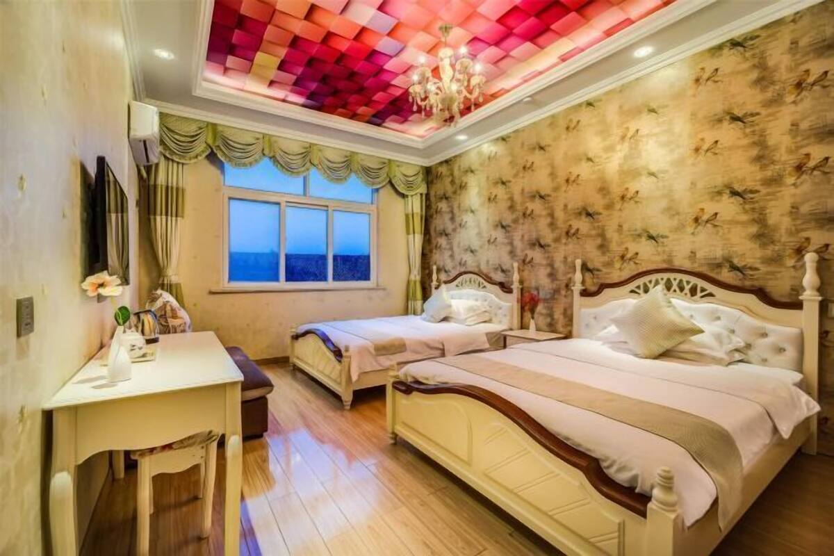 A bedroom with two beds, a desk, a window with a view, and a patterned wall.