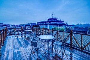 Una terraza de madera con mesas y sillas, con vistas a edificios tradicionales y una estructura de estilo pagoda.