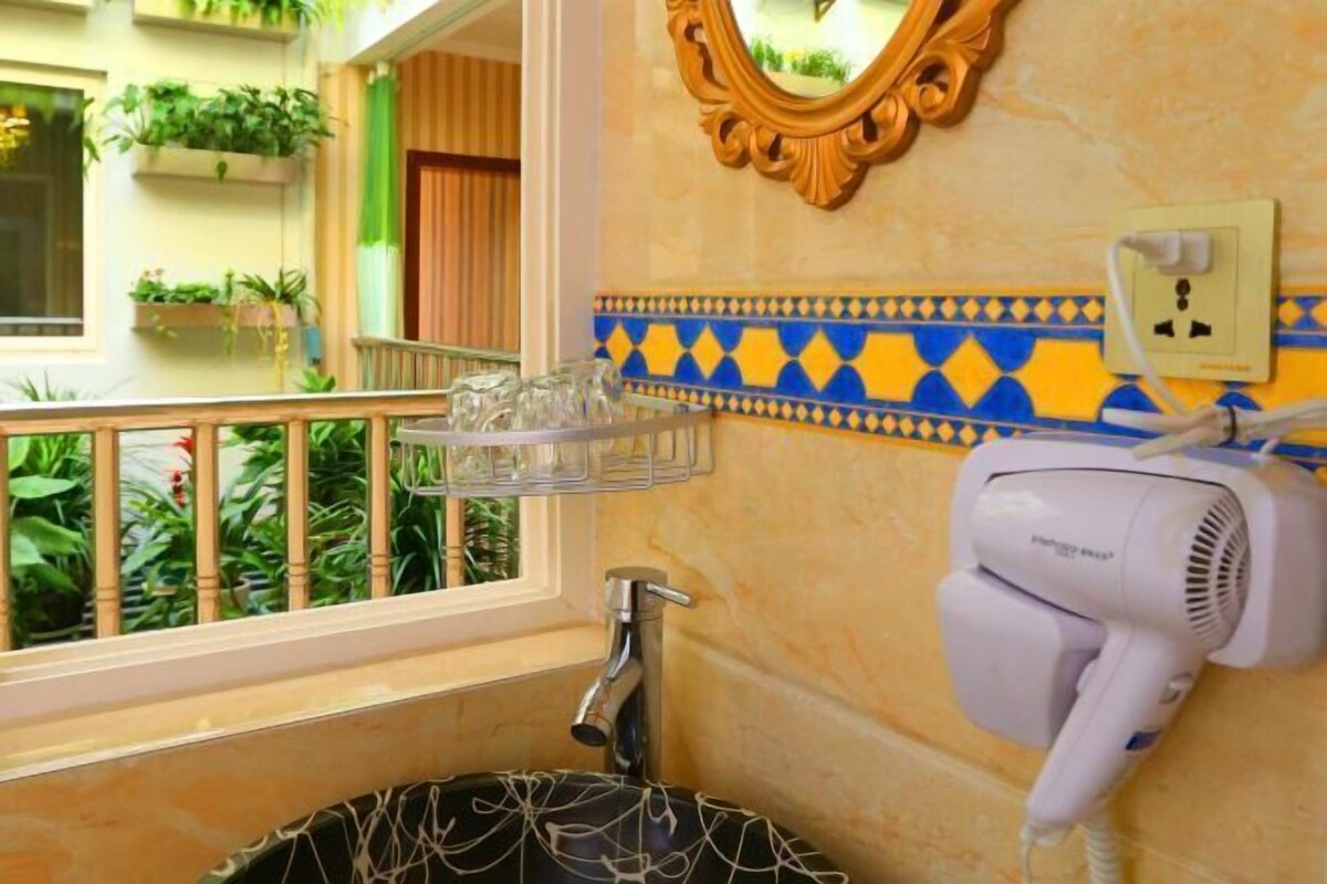 A bathroom with a sink, a hairdryer, a mirror, and a window with plants.