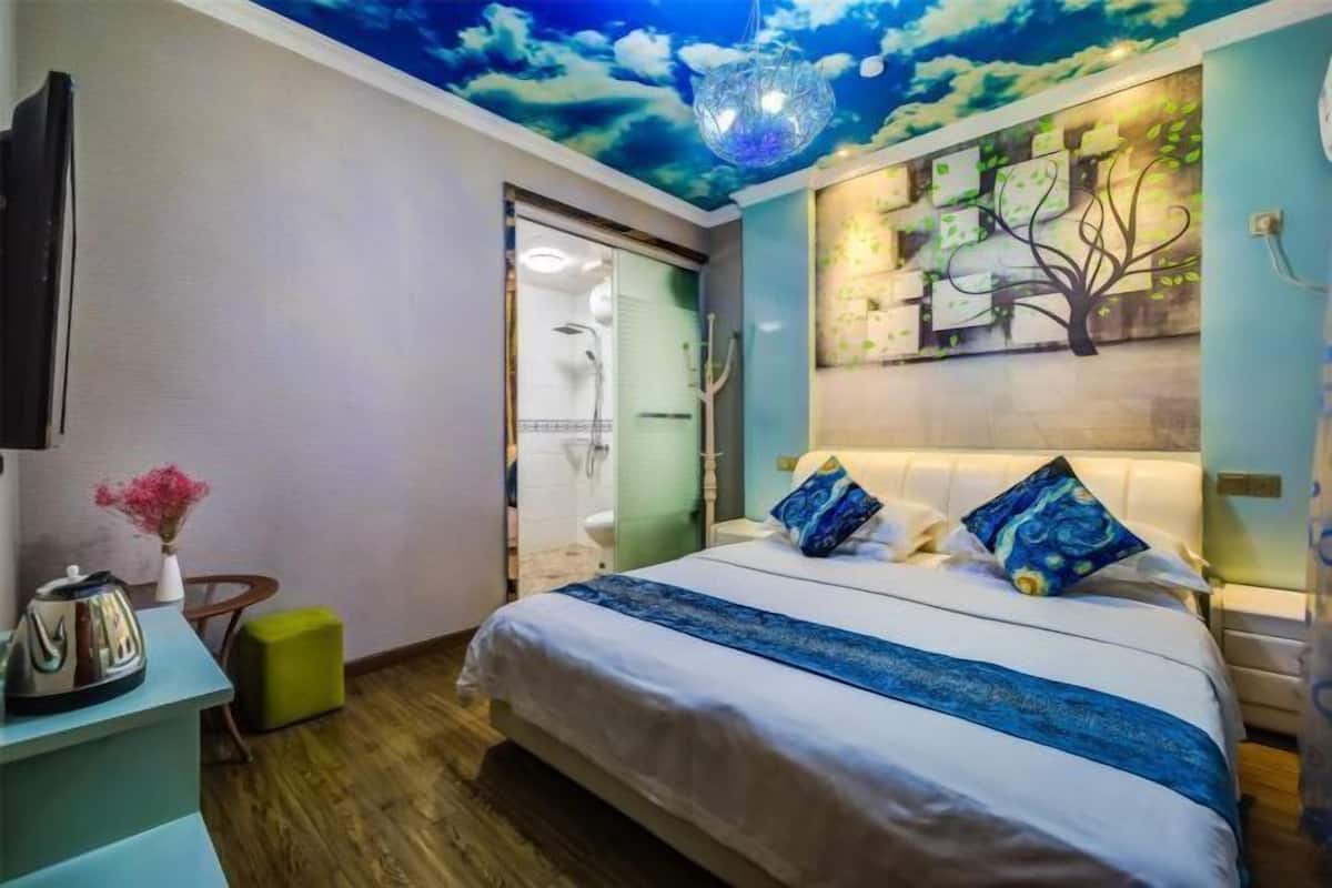 A bedroom with a bed, a nightstand, a wall-mounted TV, a ceiling mural, and a green ottoman.
