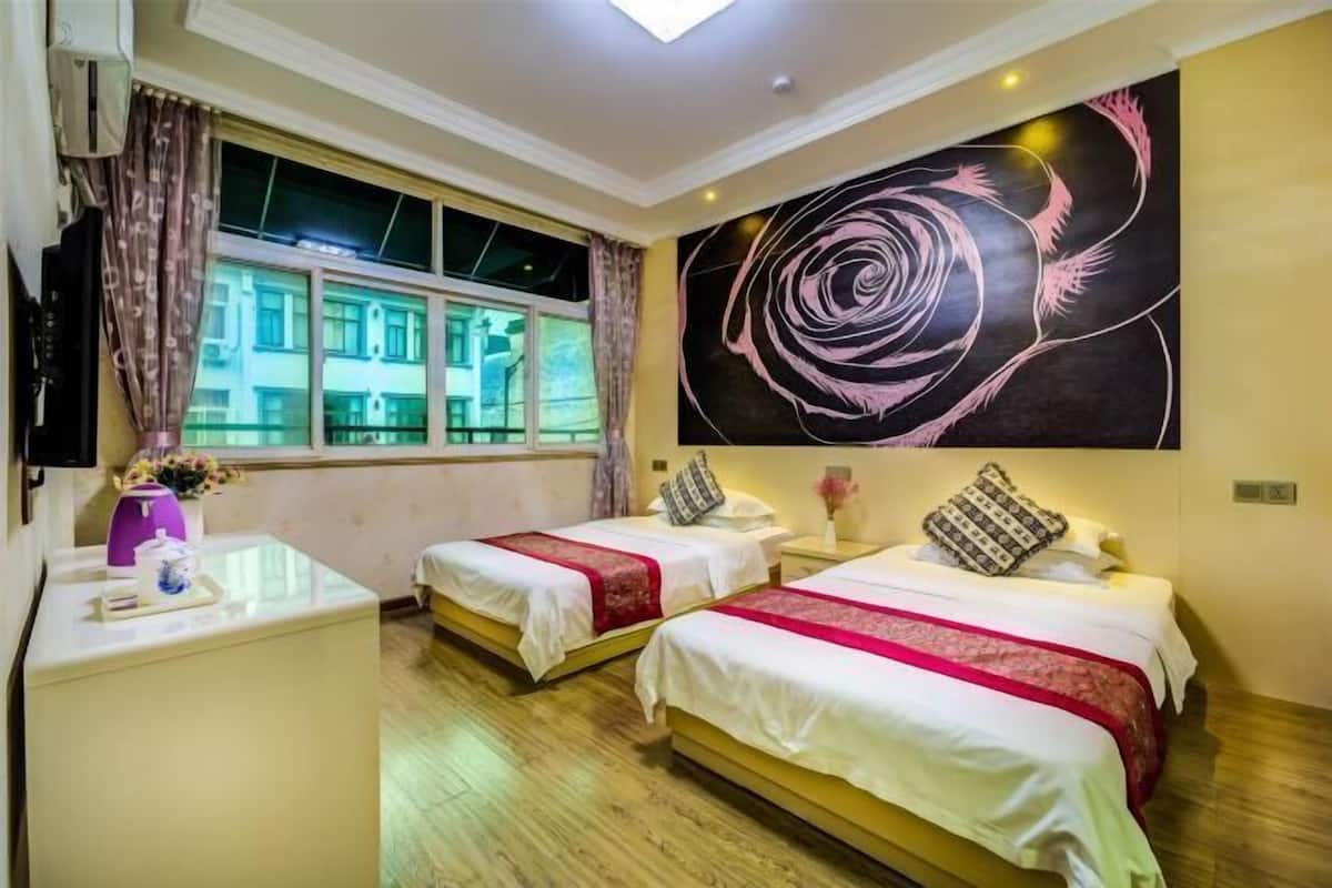 A hotel room with two beds, a large window, a wall art piece, and a flat-screen TV.