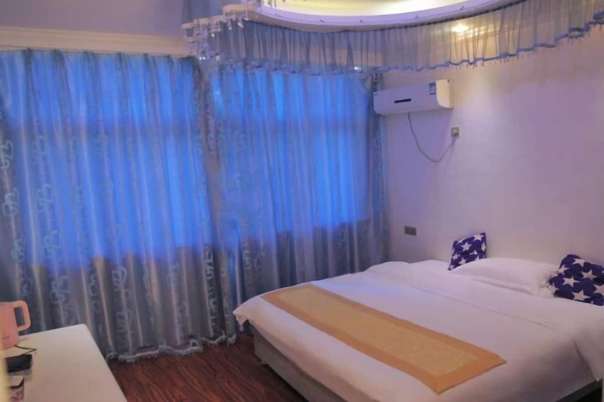 A hotel room with a bed, curtains, an air conditioning unit, and a bedside table.