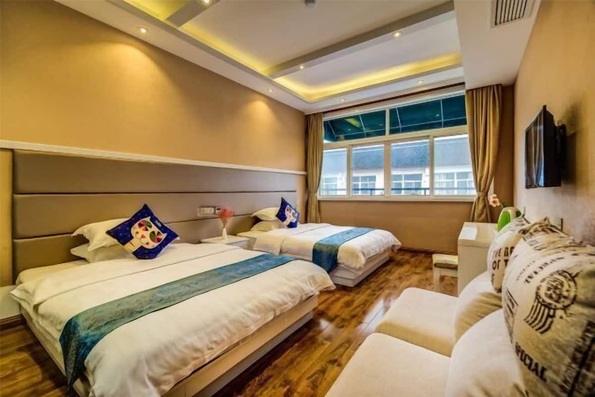 A hotel room with two beds, a sofa, a TV, and a window with curtains.