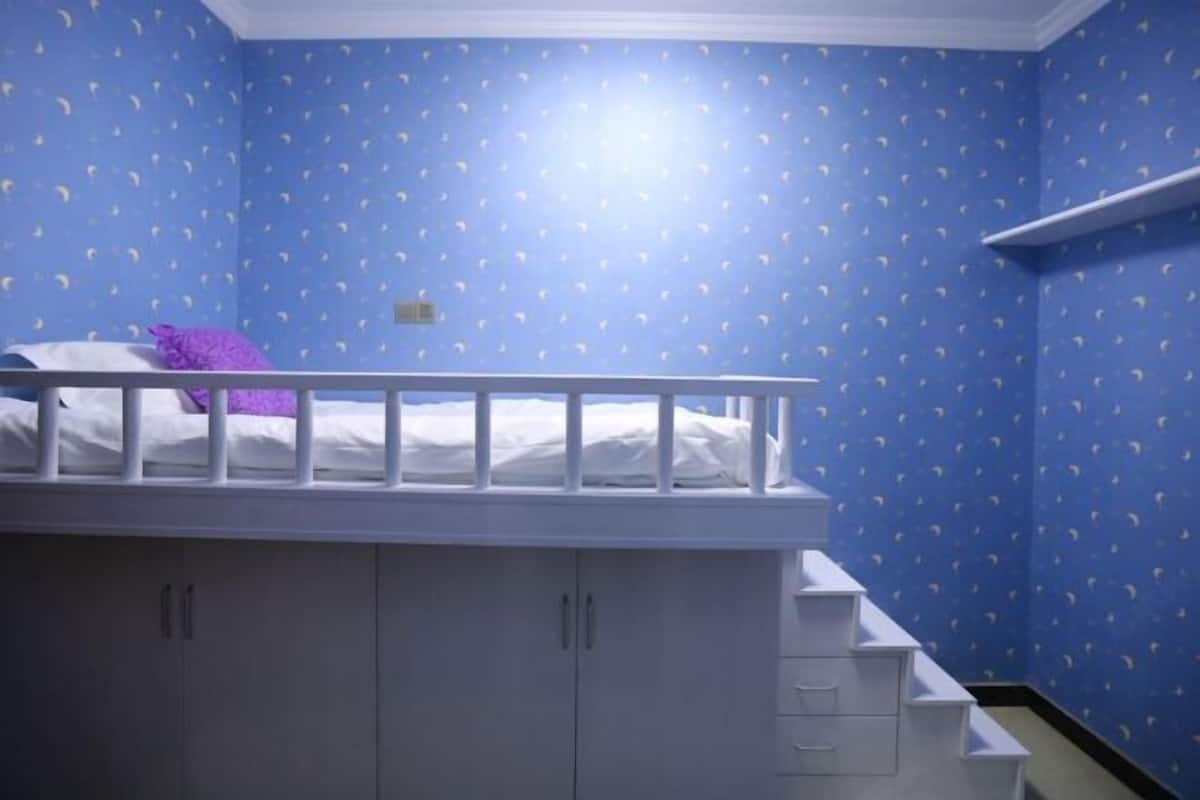 A room with a bunk bed, a white railing, and a wardrobe with multiple drawers.