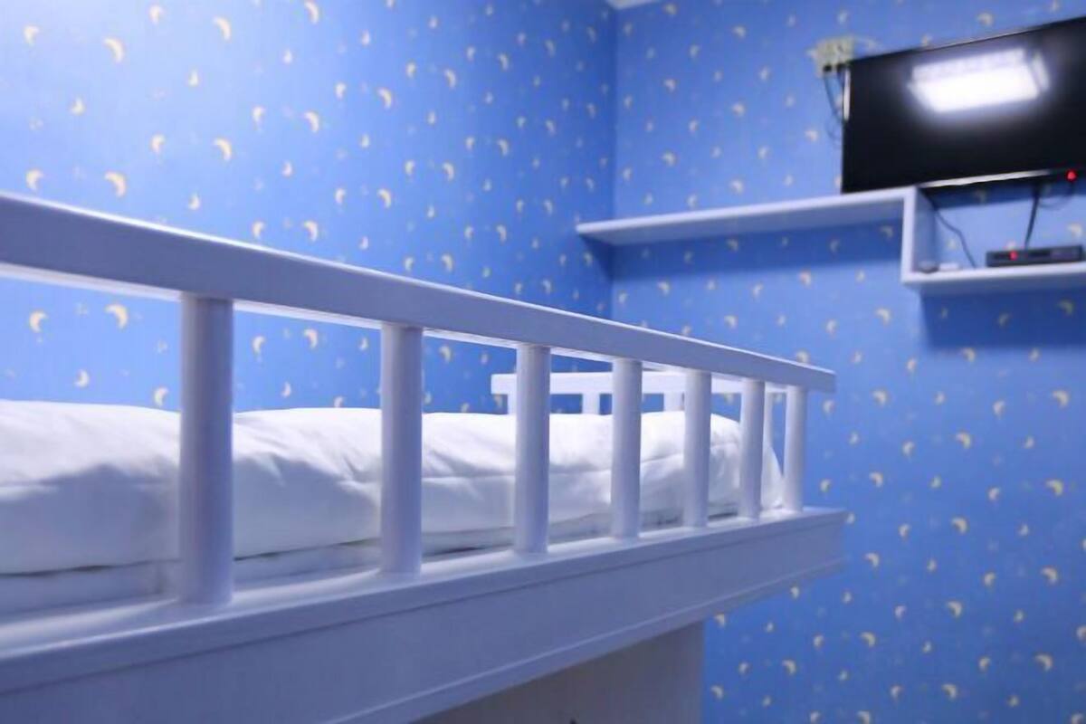 A bunk bed with a white railing, a television on a shelf, and a blue wall with a pattern.