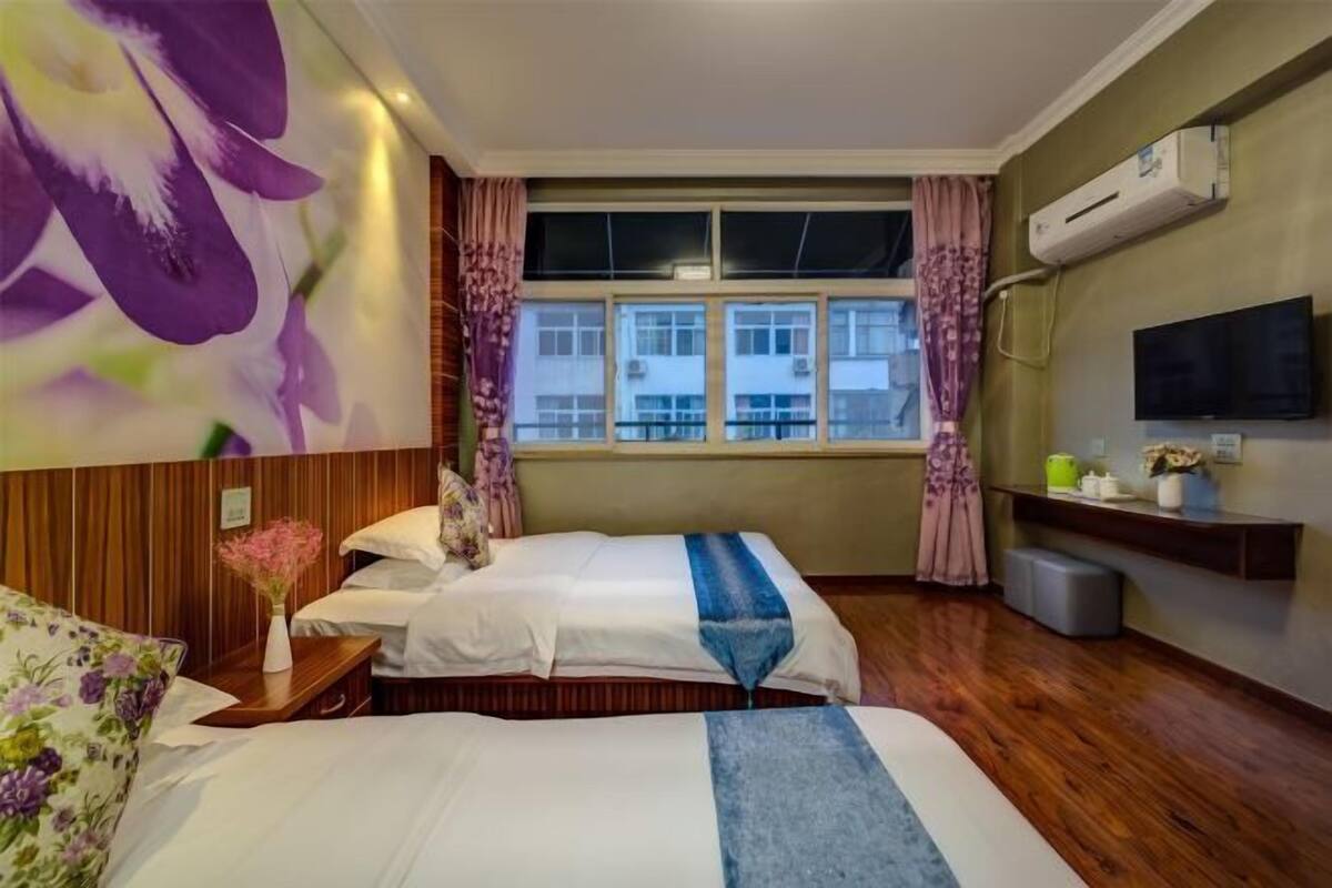 A hotel room with two beds, a TV, an air conditioner, and a window with curtains.