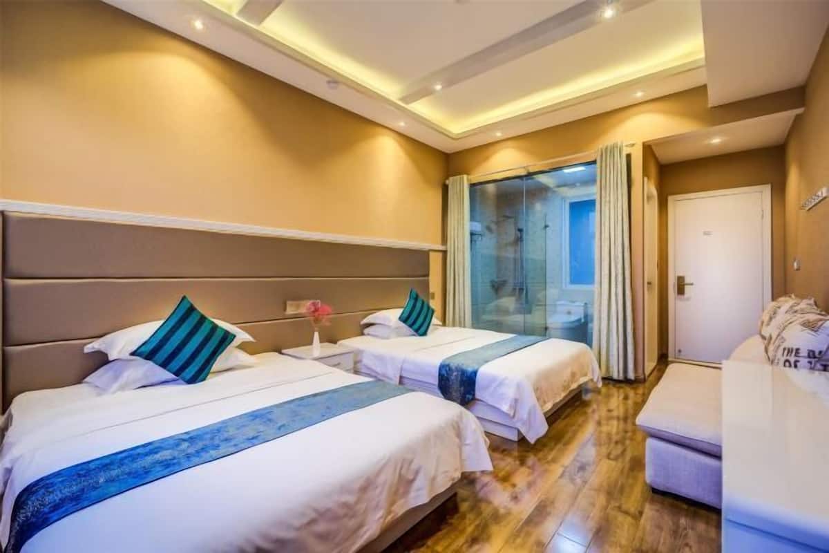 A hotel room with two beds, a sofa, a glass shower, and a door.