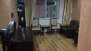 A small, cozy room with a wooden floor, a fan, a small table, two chairs, and a sofa. - Hua Yang Hotel (Yuhuan)