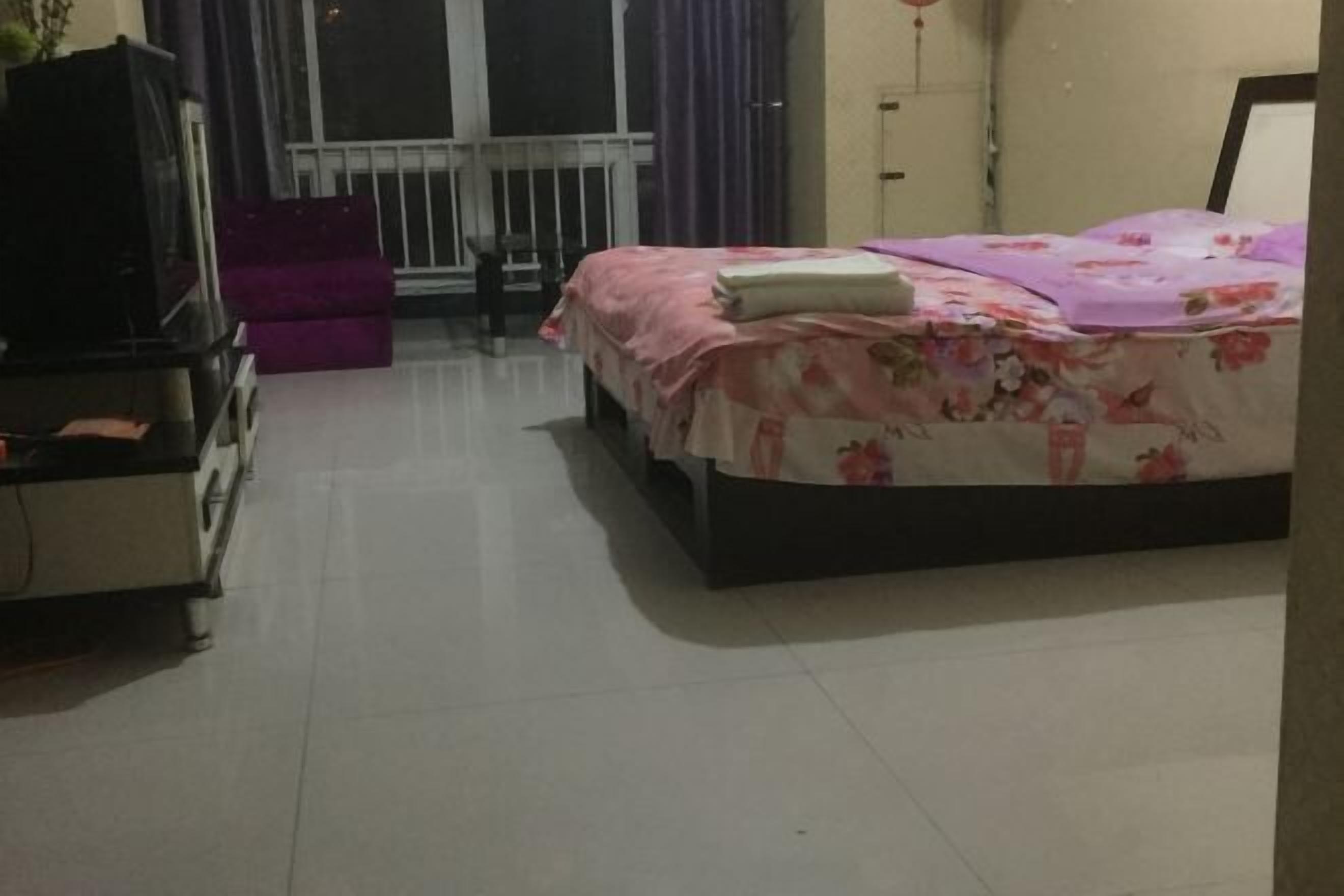 Ein Schlafzimmer mit Bett, Kommode, Fernseher und einem Fenster mit Vorhängen.