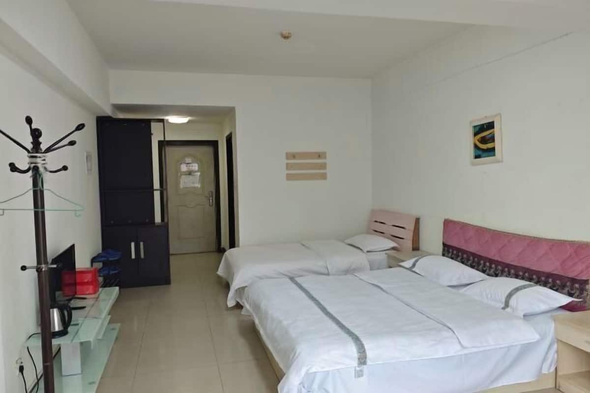 A hotel room with two beds, a wardrobe, a coat rack, and a small desk.