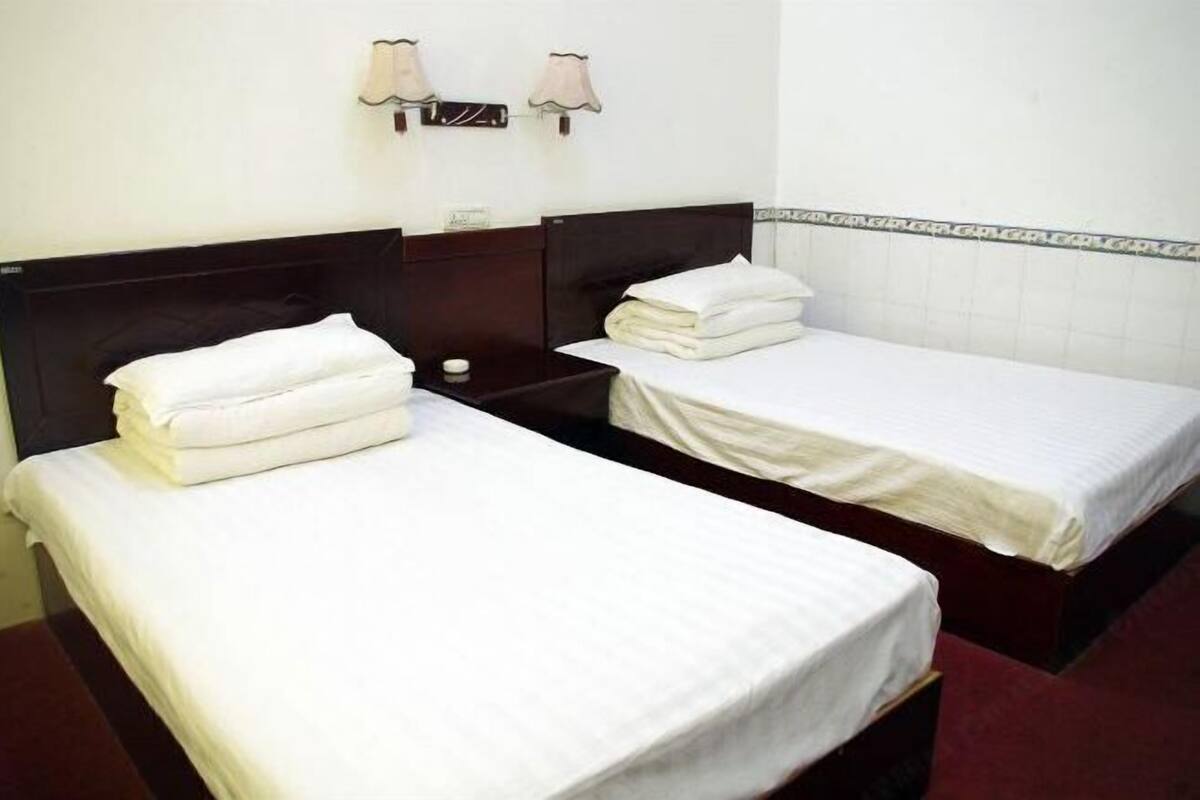 A hotel room with two single beds, a nightstand with a lamp, and a wall-mounted light fixture.