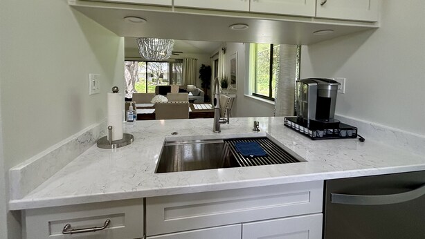 A modern kitchen with white cabinets, a stainless steel sink, and a coffee machine.