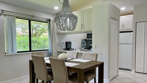 A dining area with a wooden table and chairs, a chandelier, and a view of the kitchen with appliances.