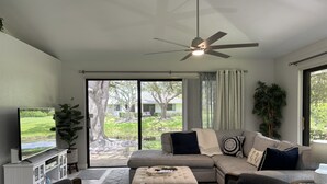 A modern living room with a sectional sofa, a flat-screen TV, and a ceiling fan.