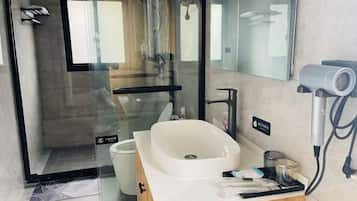 A modern bathroom with a glass shower enclosure, a white sink, and a hairdryer on the counter.