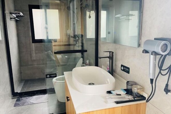 A modern bathroom with a glass shower enclosure, a white sink, and a hairdryer on the counter.