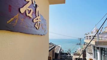 A building with a sign that includes Chinese characters, a view of the sea, and a cable car in the distance.