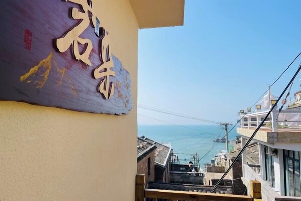 A building with a sign that includes Chinese characters, a view of the sea, and a cable car in the distance.
