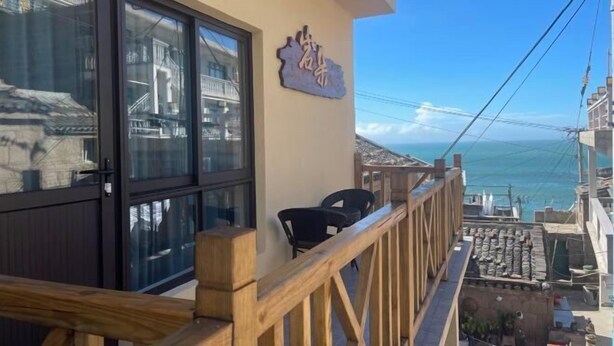A balcony with a wooden railing, a glass door, and a view of the sea. - Zhoushan Dongji Yanduo Homestay (Dongfushan Branch) (Zhoushan)