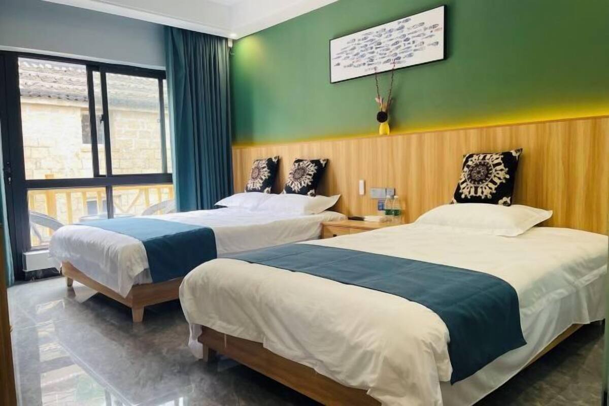 Habitación de hotel con dos camas, un ventanal grande y una pared verde.