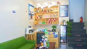 A reception area with a green sofa, a wooden table with a vase, a shelf with various bottles, a chalkboard, and a staircase with signs. - Zhoushan Dongji Yanduo Homestay (Dongfushan Branch) (Zhoushan)