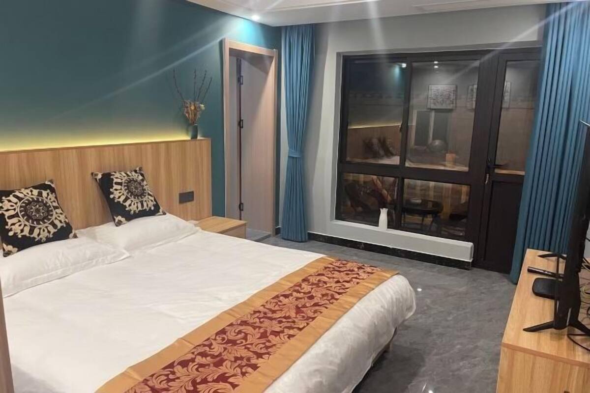 Una habitación de hotel con una cama grande, un escritorio con computadora, una ventana que ofrece vistas al exterior y una puerta que da a otra habitación.