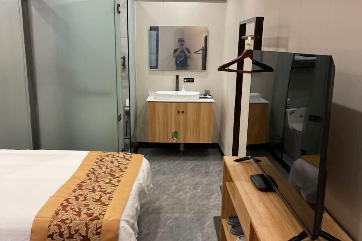 A hotel room with a bed, a wooden cabinet with a mirror, a sink, and a television.