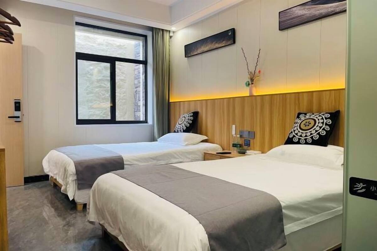 Habitación de hotel con dos camas, una ventana, una obra de arte colgada en la pared y una mesita de noche con una lámpara.