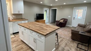Amplia sala de estar con isla de cocina, un sofá de cuero marrón y un televisor.