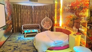 A hotel room with a bed, a sofa, a fan, a small table, and a wall with a painting. - Concept hotel (Ziyang)