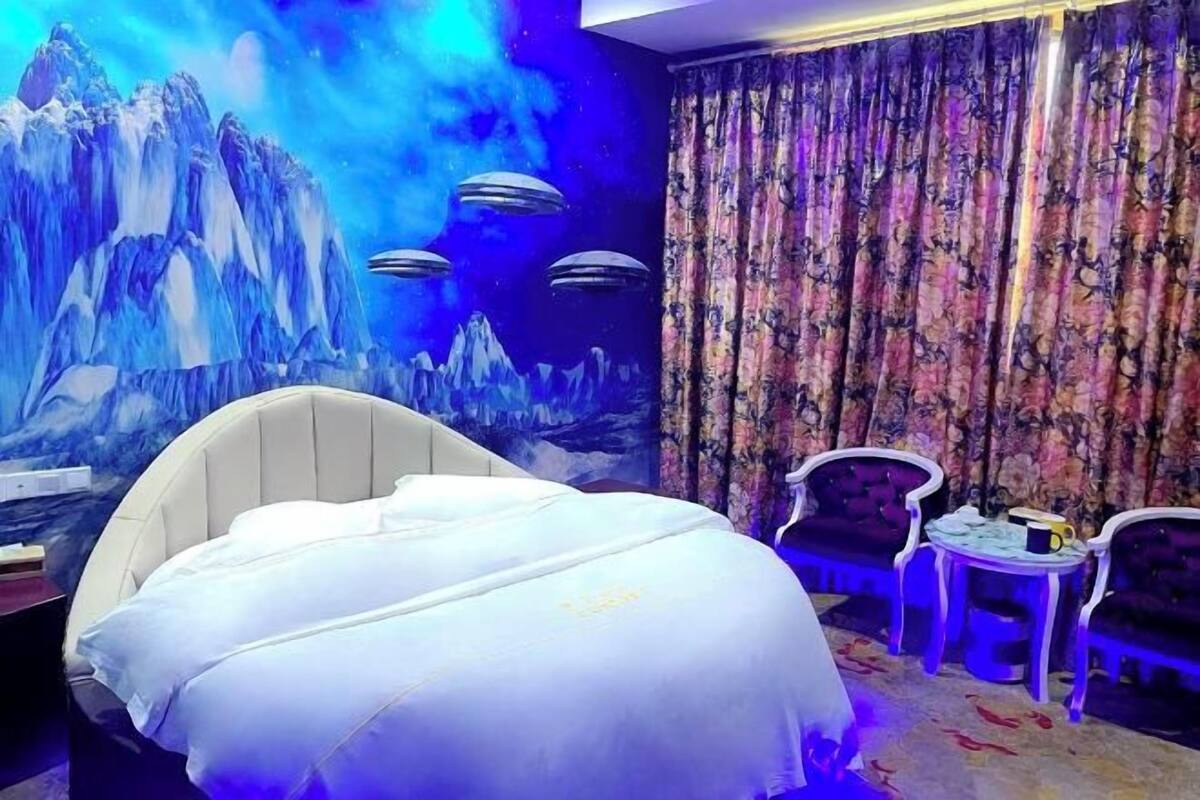 Una habitación con una cama, un mural de montañas y OVNIs, una cortina floral y dos mesitas.