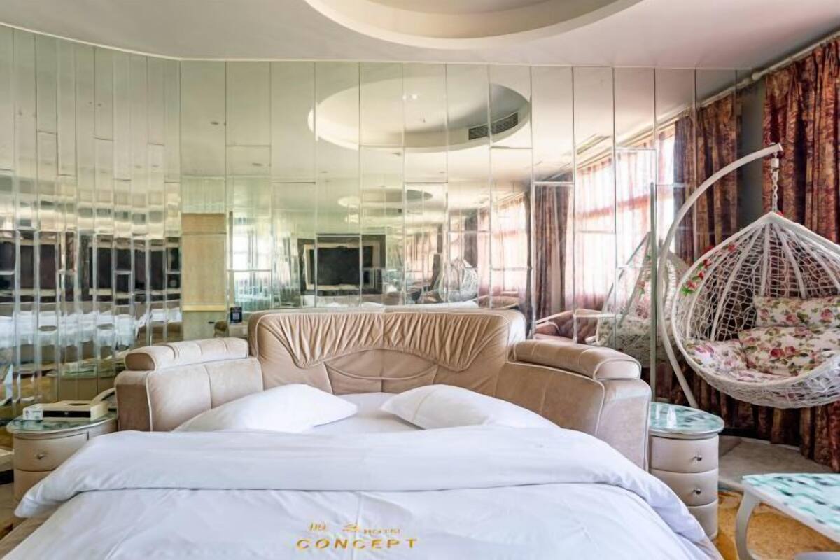 Una habitación de hotel moderna con una cama grande, una silla colgante y un muro de vidrio.