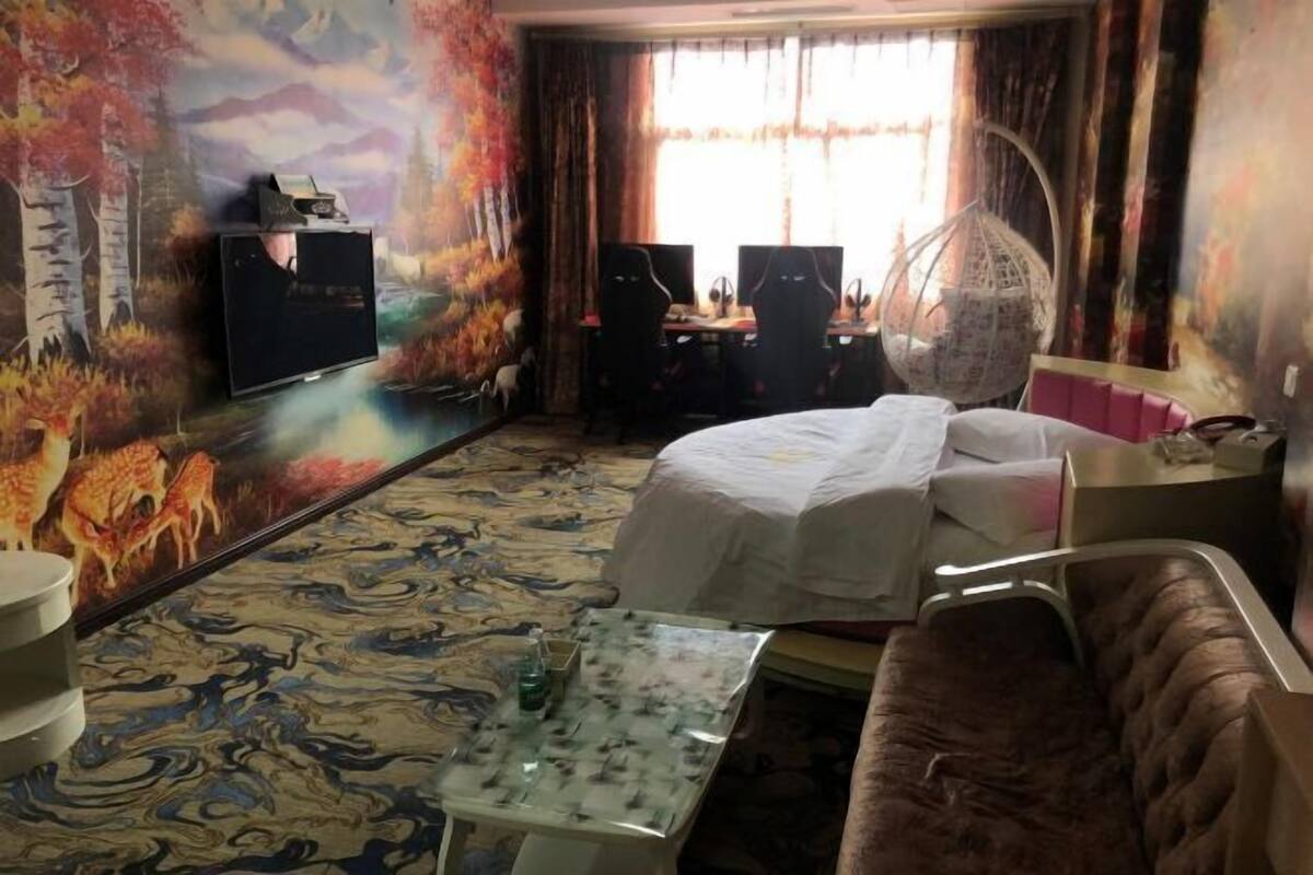 Habitación de hotel con cama, un escritorio y dos sillas, televisión y un mural decorativo en la pared.