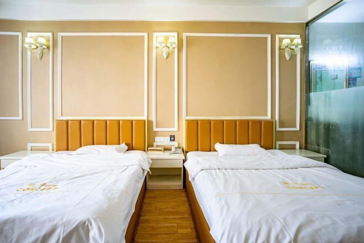 A hotel room with two beds, a wooden floor, and wall-mounted lamps.