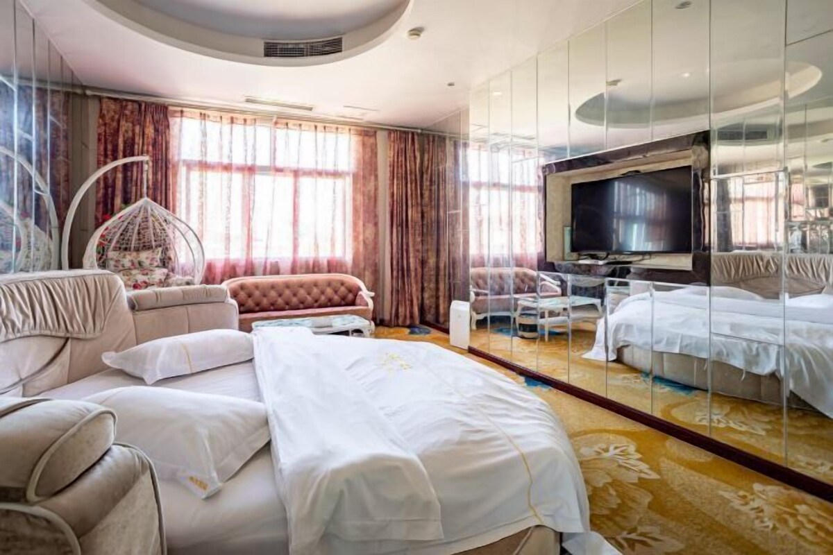 A hotel room with a large bed, a sofa, a television, and a glass partition.