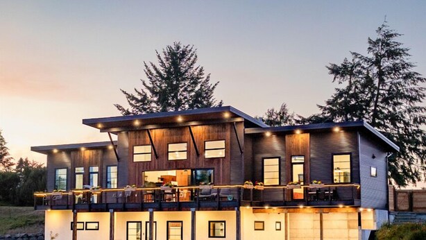 Une maison moderne à deux étages, dotée d’une grande terrasse, de nombreuses fenêtres et d’un garage.