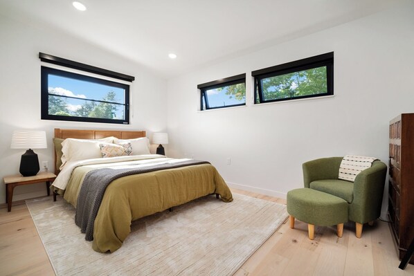 A bedroom with a bed, two bedside tables, a chair, and two windows. - Modern Chalet Lux Home with Mnt Views, Hot Tub & EV Charger (Sequim)