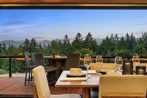 An outdoor dining area with wicker chairs and a wooden table set for a meal, overlooking a forested mountain range. - Modern Chalet Lux Home with Mnt Views, Hot Tub & EV Charger (Sequim)