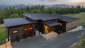 Una casa moderna de dos pisos con techo metálico, fachada de madera y un camino de entrada a un acceso con portón.