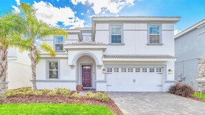 A two-story house with a white exterior, a front entrance with a dark door, a garage, and a well-maintained lawn. - Champions Gate Resort Home w BBQ Pool  (Davenport)