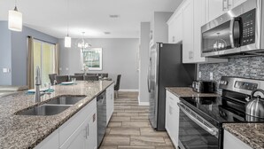 A modern kitchen with granite countertops, stainless steel appliances, and a tiled backsplash. - Champions Gate Resort Home w BBQ Pool  (Davenport)