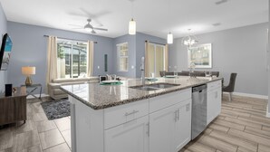 A modern kitchen with a central island, white cabinetry, and a large window providing natural light. - Champions Gate Resort Home w BBQ Pool  (Davenport)