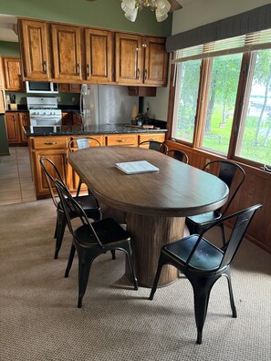 A kitchen with wooden cabinets, a dining table with chairs, and a view of the outdoors through large windows. - "Villa Lago" Charming 4 bedroom 3 bath Farm Island Lake home with 3 fire places (Aitkin)