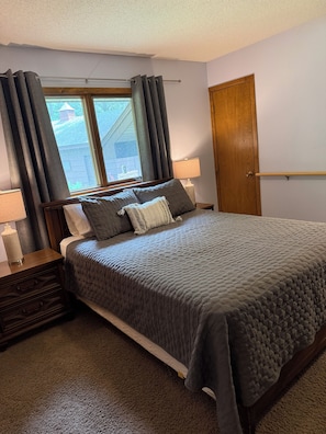 Une chambre à coucher avec un lit, des tables de chevet, une fenêtre avec des rideaux, une porte et une lampe.